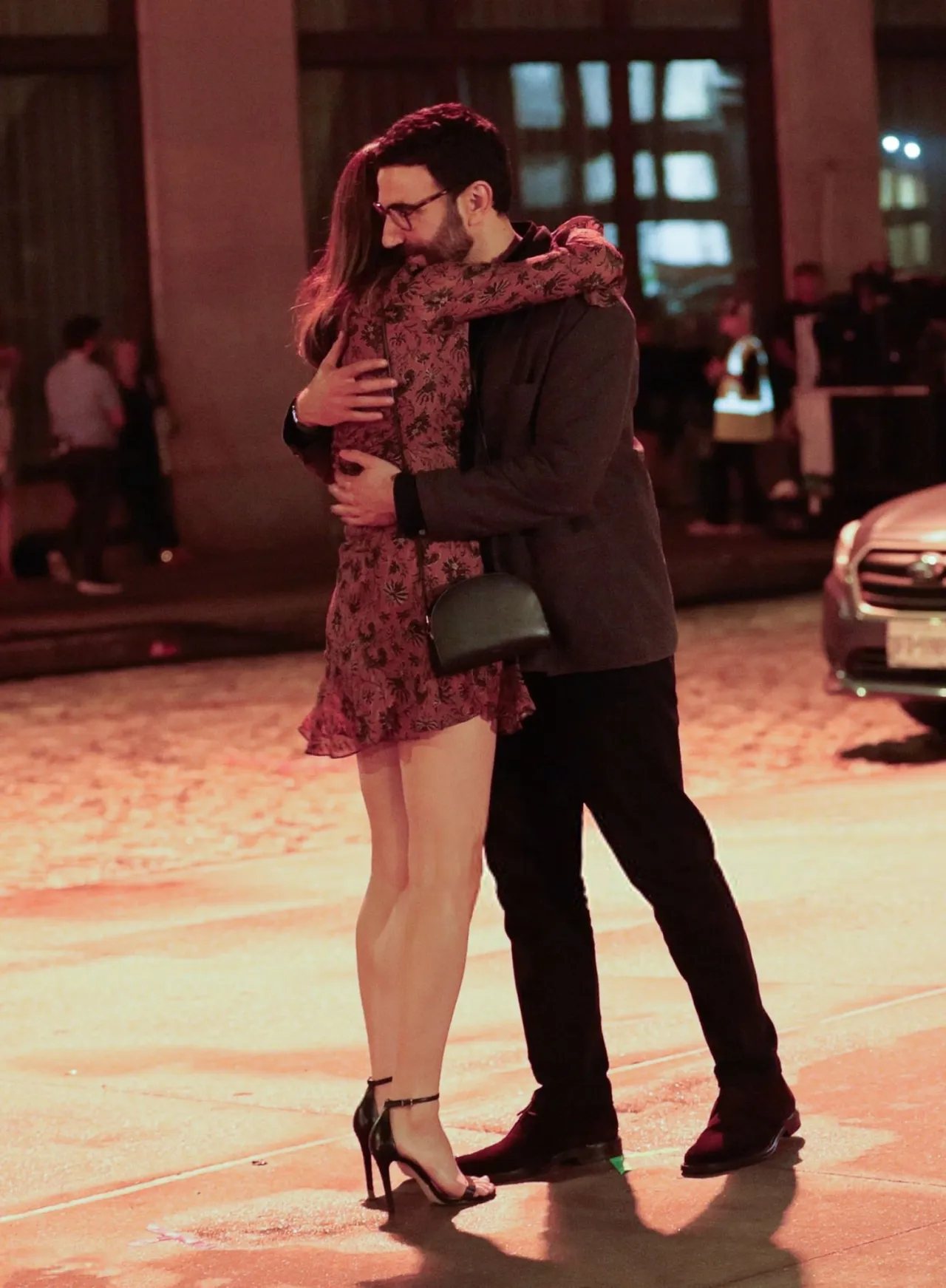 Alexandra Daddario embracing a man on a wet Tribeca street at night, short dress and heels