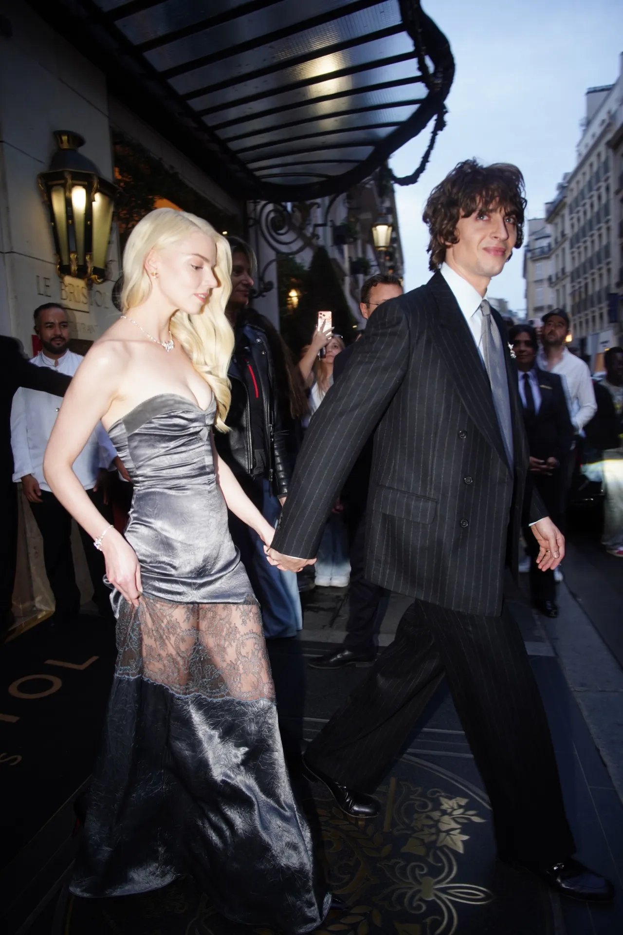 Anya Taylor-Joy in a sheer silver dress leaving her Paris hotel with Malcolm McRae, 2026