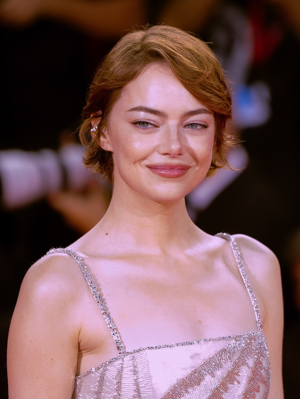 Emma Stone smiling on the red carpet in a pale pink beaded slip dress at the Venice Film Festival premiere of Bugonia, 2025