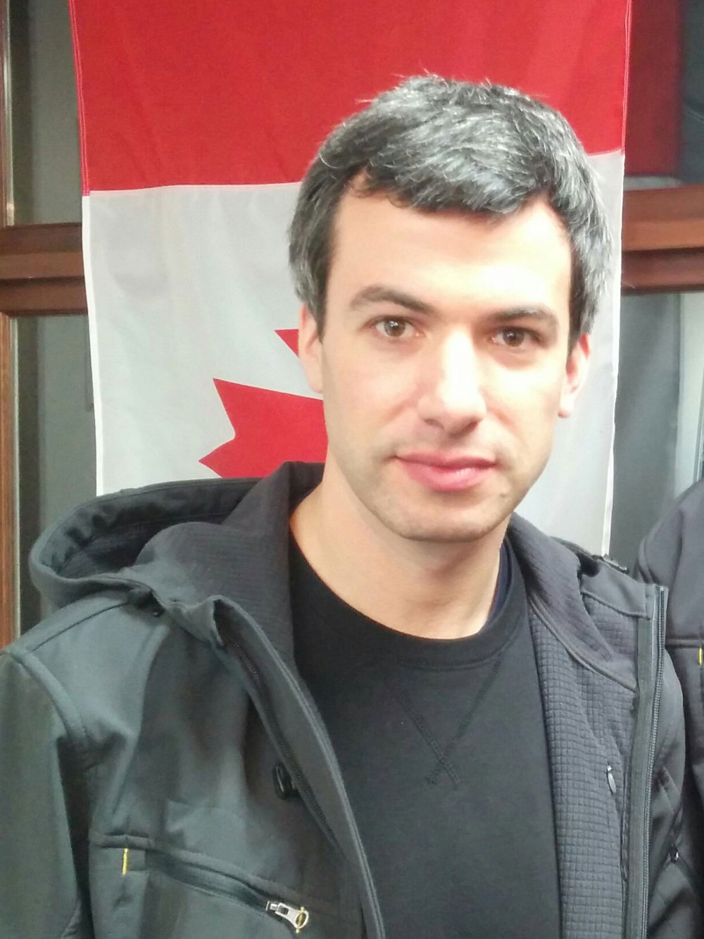 Nathan Fielder in a dark jacket in front of a Canadian flag at a Summit Ice pop-up in Vancouver, 2017