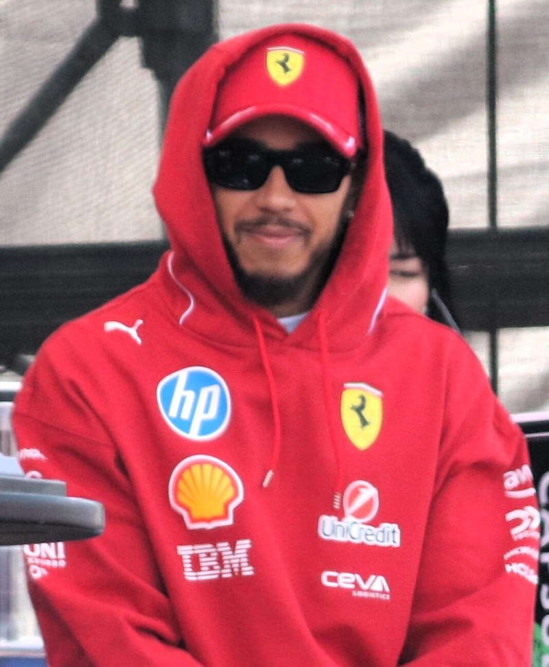 Lewis Hamilton in a red Ferrari hoodie and cap on the fan zone stage at the 2025 Japanese Grand Prix