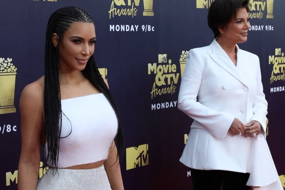 Kim Kardashian with long braids in a white strapless crop top next to Kris Jenner in a white suit at the 2018 MTV Movie and TV Awards