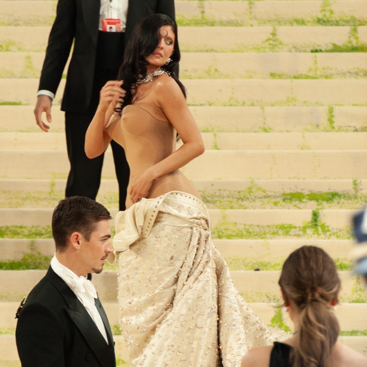 Kylie Jenner walking up the steps at the 2026 Met Gala in a nude corset gown with ivory train
