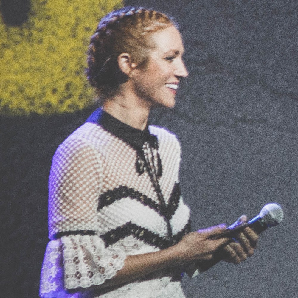 Brittany Snow smiling onstage with a microphone at a Pitch Perfect 3 cast event, 2017